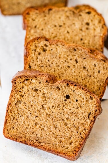 Three thick slices of banana bread stacked on white parchment paper.
