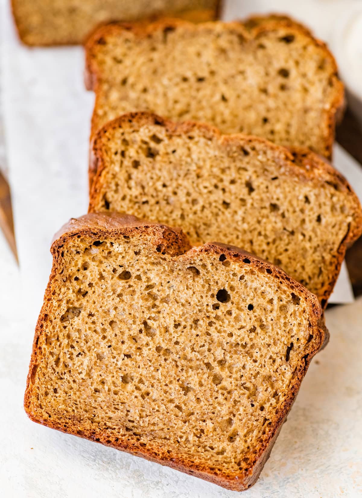 Three thick slices of banana bread stacked on white parchment paper.