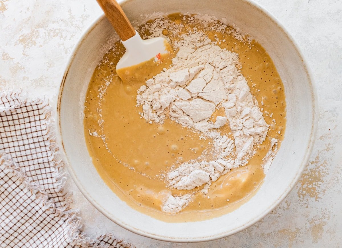 Mixing bowl with wet banana bread ingredients and flour being folded in.