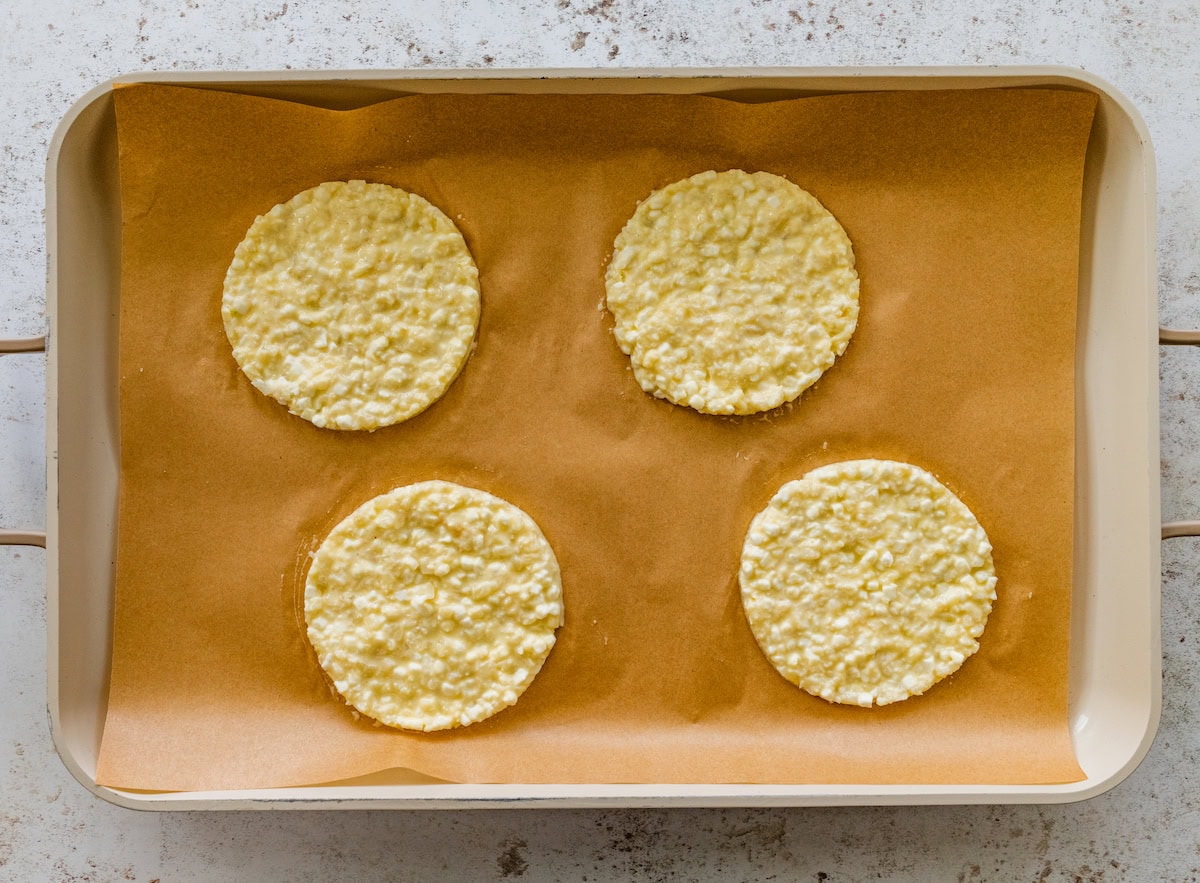 Four un-baked cauliflower thins spread out on a baking sheet lined with parchment paper.