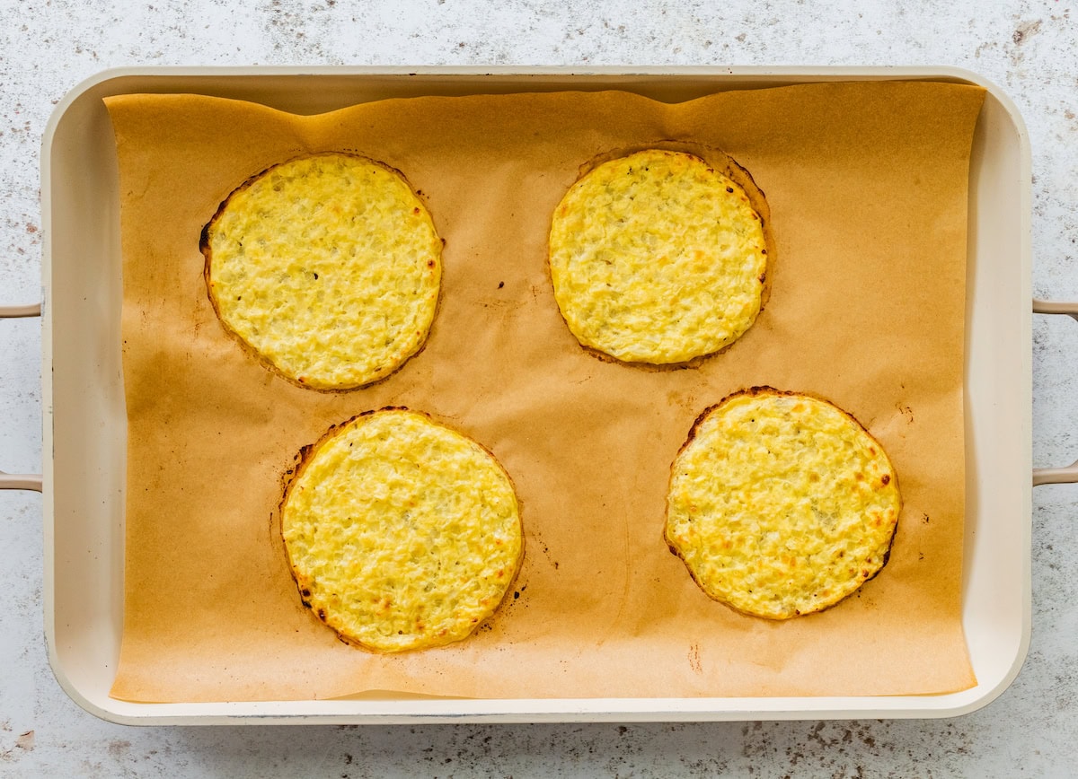 Four baked cauliflower thins spread out on a baking sheet lined with parchment paper.