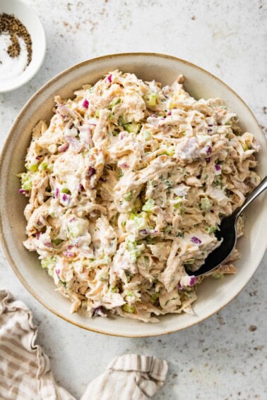 Cottage cheese chicken salad served in a cream bowl with a spoon. There is a small bowl with salt and pepper next to it.