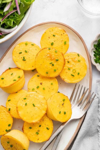 12 cottage cheese egg bites on a white serving plate topped with chopped chives. There are two forks on the plate.