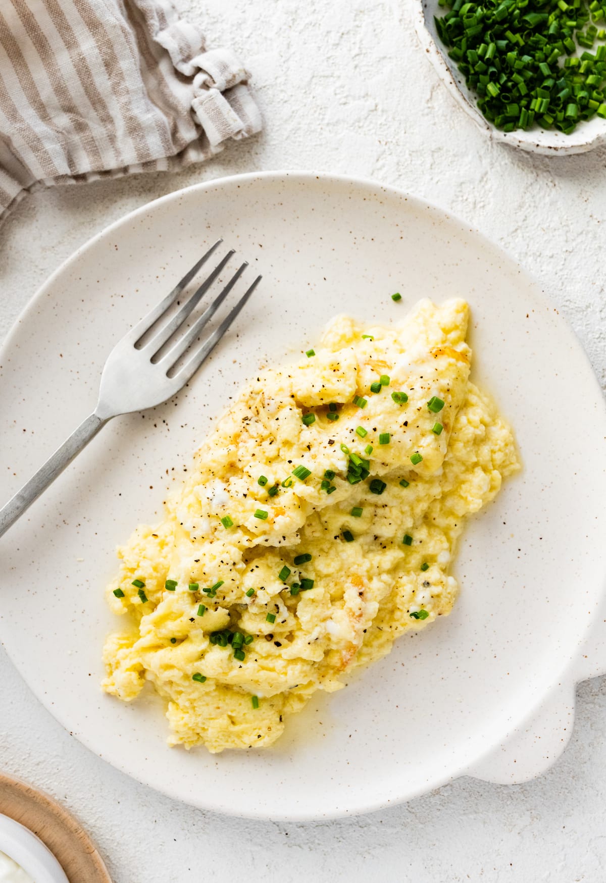 Cottage cheese scrambled eggs on a plate garnished with fresh chives, salt, and pepper.