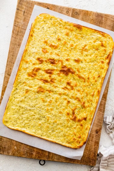 A baked cottage cheese flatbread on parchment paper on top of a wooden cutting board.