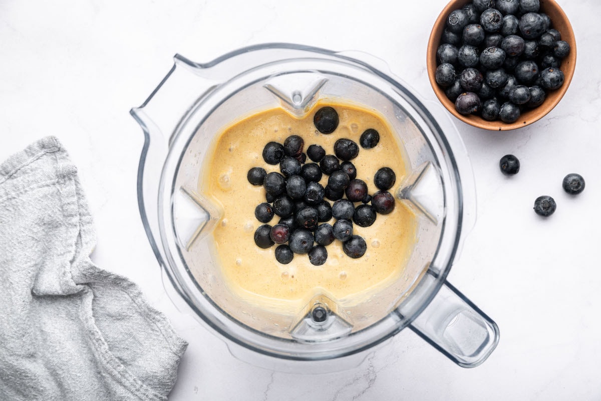 Fresh blueberries being added to a Vitamix blender with the cottage cheese muffin mixture.