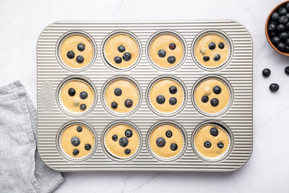 12 unbaked blueberry cottage cheese muffins in silicone liners in a muffin tin.