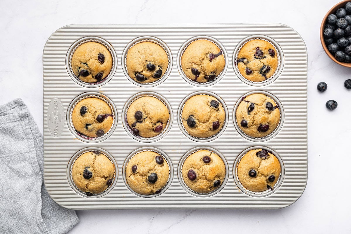 12 baked blueberry cottage cheese muffins in silicone liners in a muffin tin.