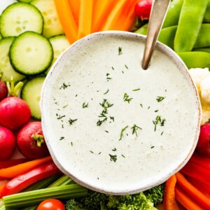 Cottage cheese ranch dip in a white bowl garnished with fresh dill. The bowl is on a plate with an assortment of fresh vegetables.