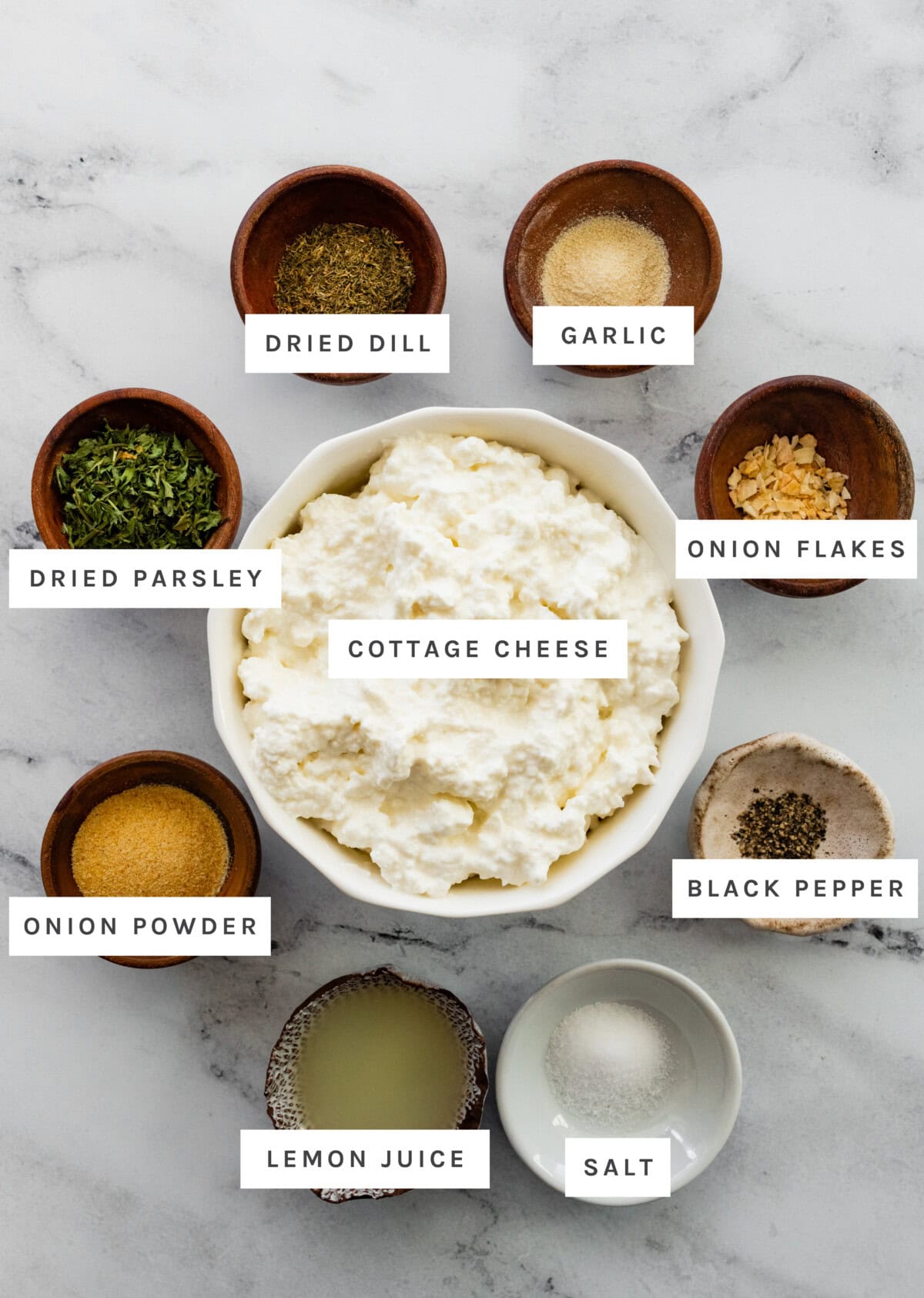 ingredients measured out to make Cottage Cheese Ranch Dip: cottage cheese, dried dill, garlic, onion flakes, black pepper, salt, lemon juice, onion powder, and dried parsley. Let me know if you need help with a recipe or editing the image!