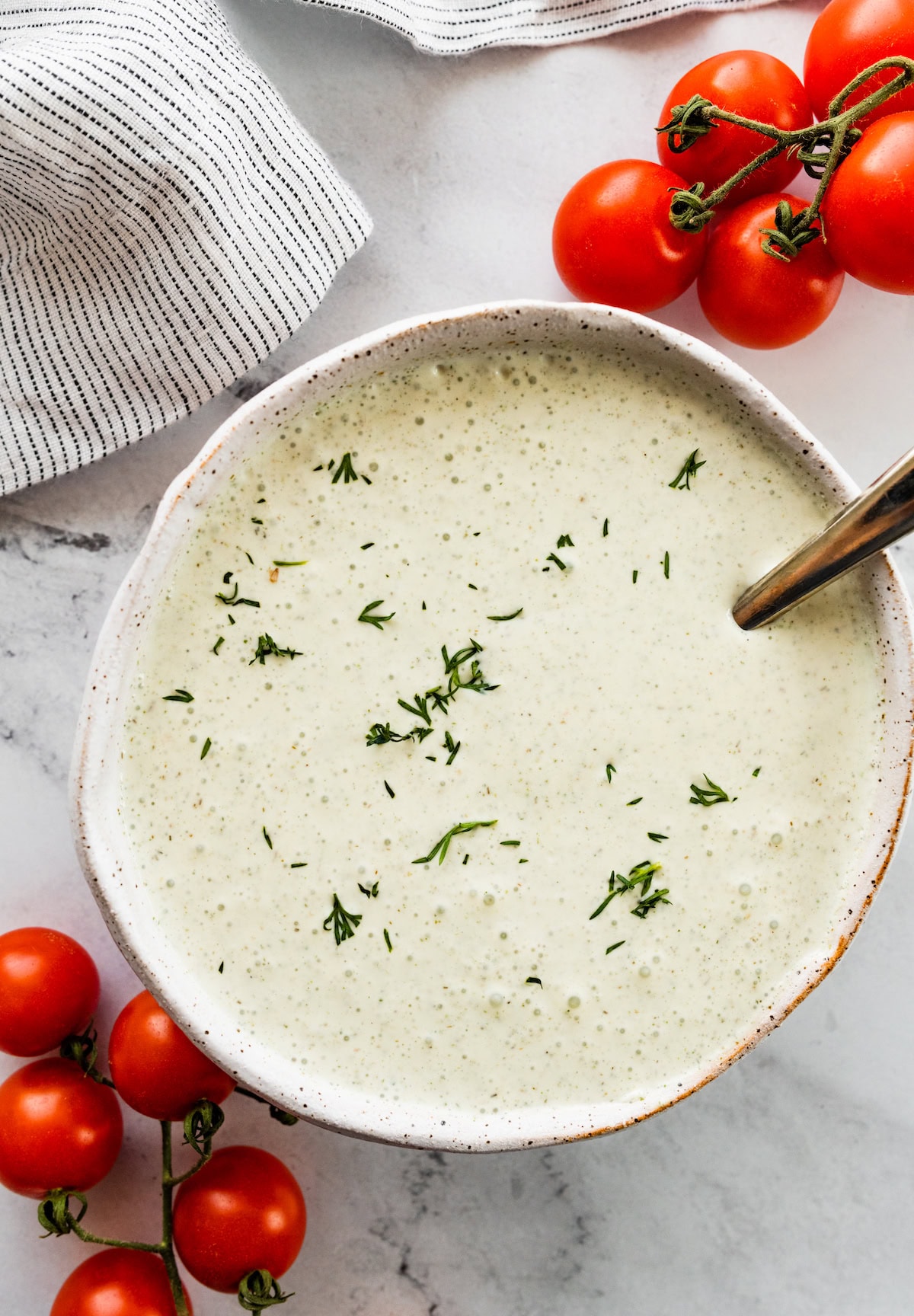 A white bowl of cottage cheese ranch dip garnished with fresh dill. To each side of the bowl are fresh cherry tomatoes.