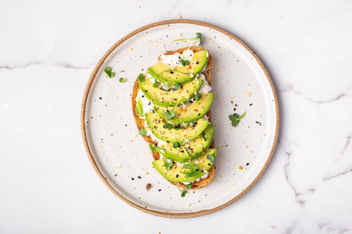 Cottage cheese toast topped with sliced avocado, flaky sea salt, cracked pepper, and fresh herbs.