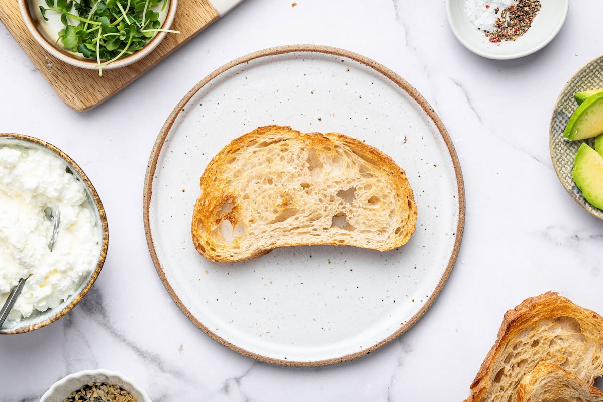Single slice of toasted sourdough bread on a white speckled plate.