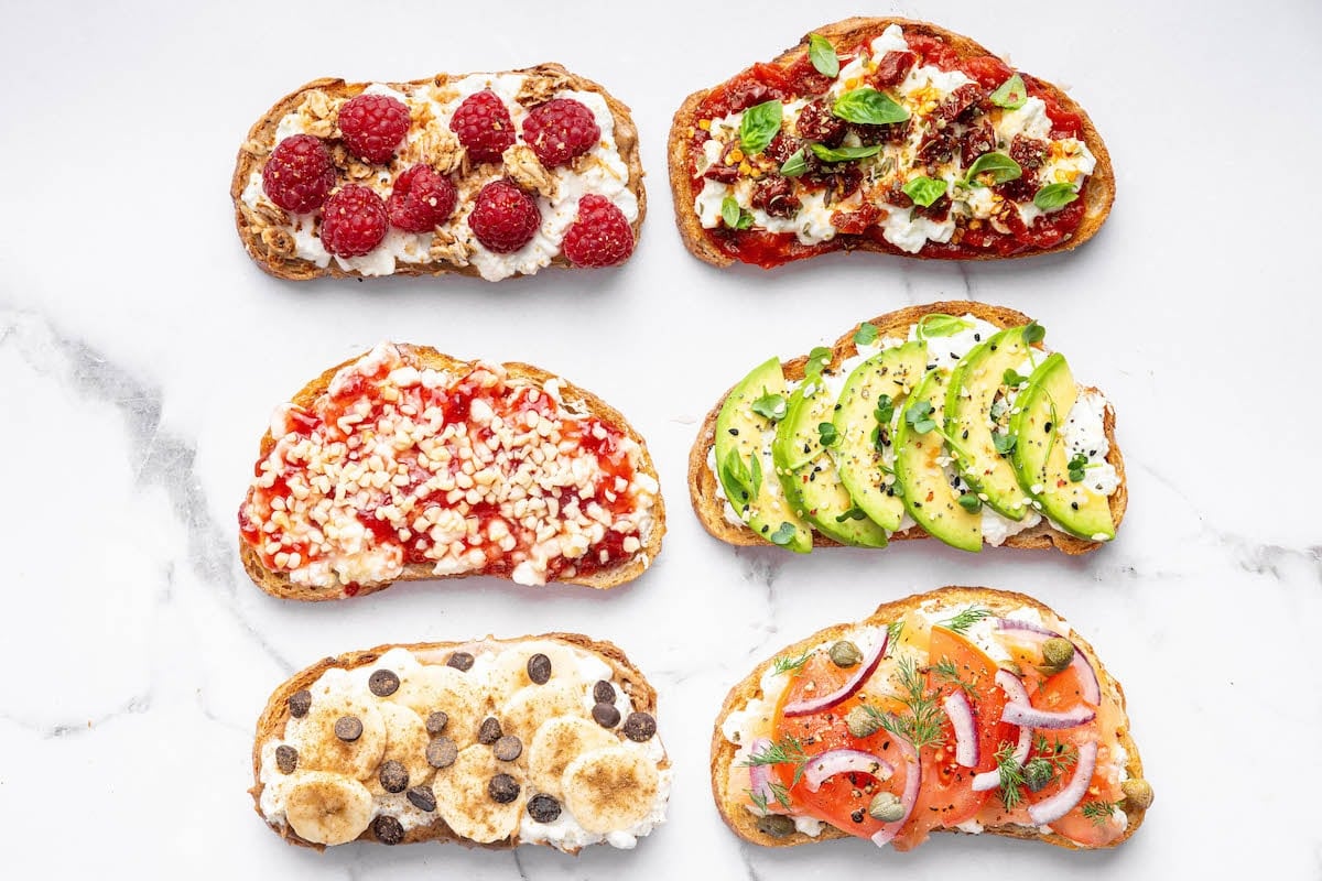 Six variations of cottage cheese toast including avocado, smoked salmon, pizza, berry jam with nuts, cinnamon banana with chocolate chips, and berries with granola on a white background.