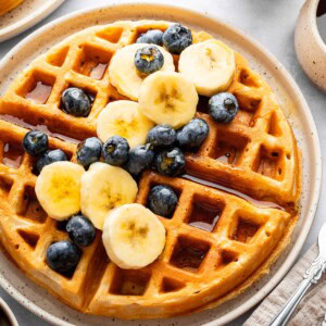 Golden brown cottage cheese waffle topped with banana slices and blueberries on a plate.