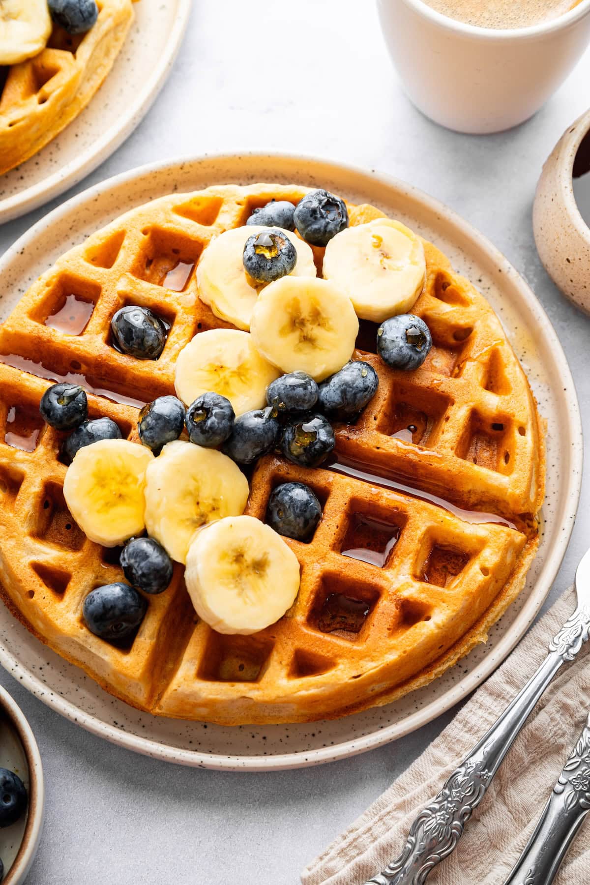 Golden brown cottage cheese waffle topped with banana slices and blueberries on a plate.