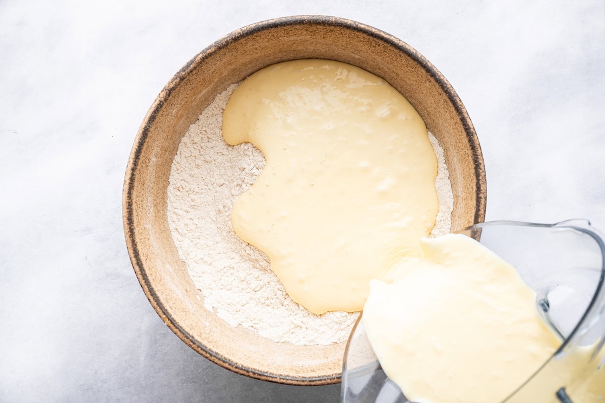 Pouring blended wet ingredients into a bowl of dry ingredients for cottage cheese waffles.