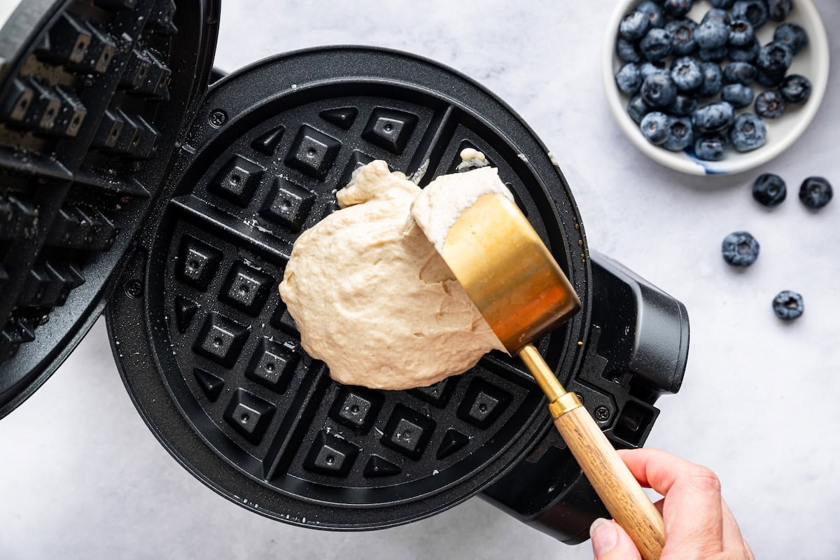 Pouring cottage cheese waffle batter into a preheated waffle maker with a measuring cup.