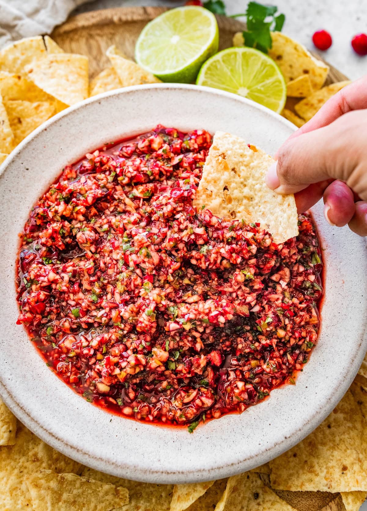 Dipping a tortilla chip into cranberry salsa, showing the chunky texture and bright colors.