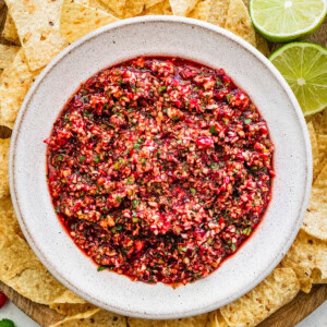 Fresh cranberry salsa served in a white bowl on a wooden tray surrounded by tortilla chips for serving.
