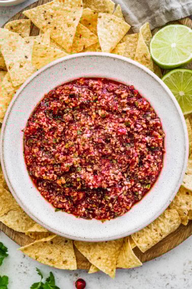 Fresh cranberry salsa served in a white bowl on a wooden tray surrounded by tortilla chips for serving.