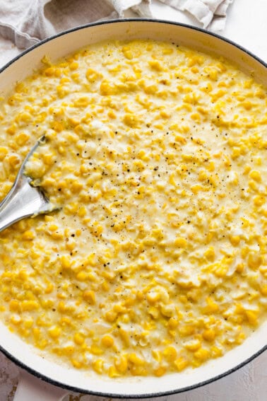Creamed corn served in a white skillet with a silver spoon topped with freshly cracked pepper.