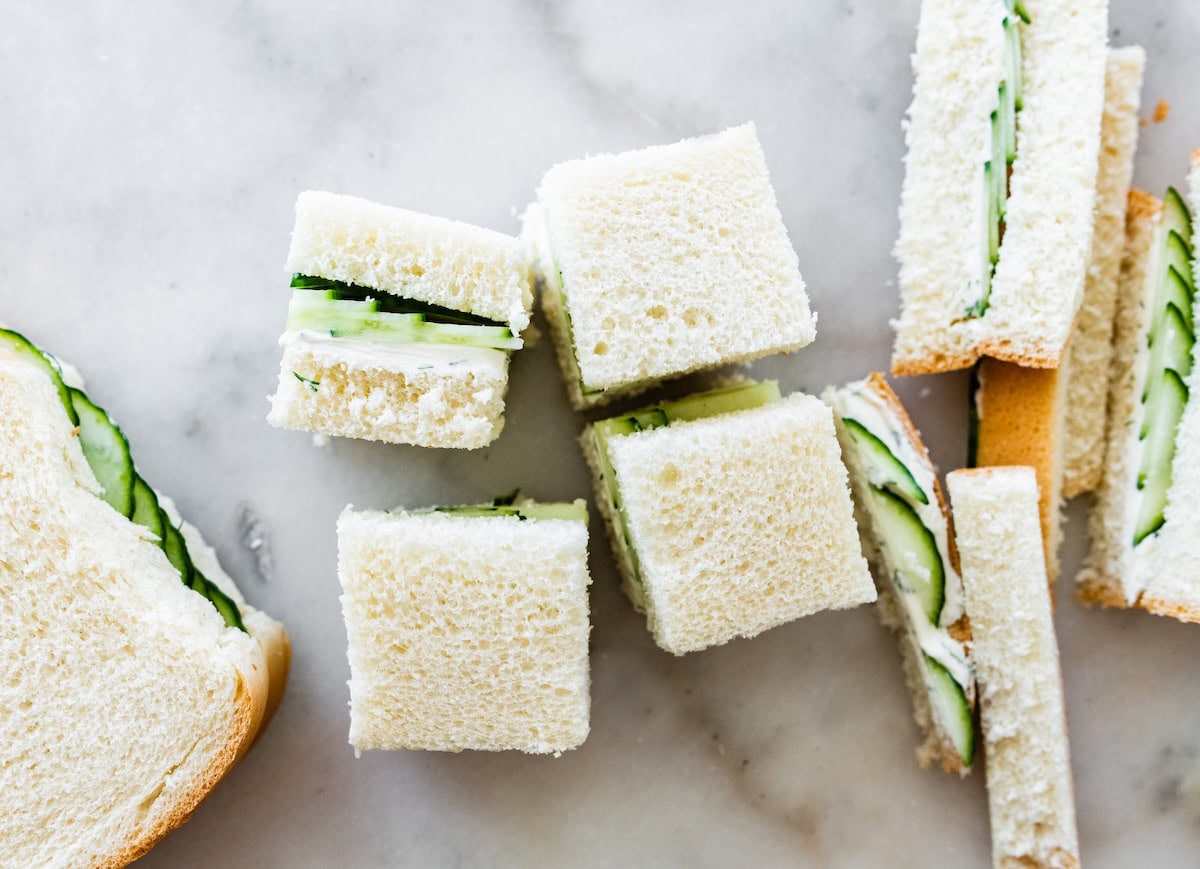 Stack of crustless cucumber sandwiches cut into small squares on a marble surface.