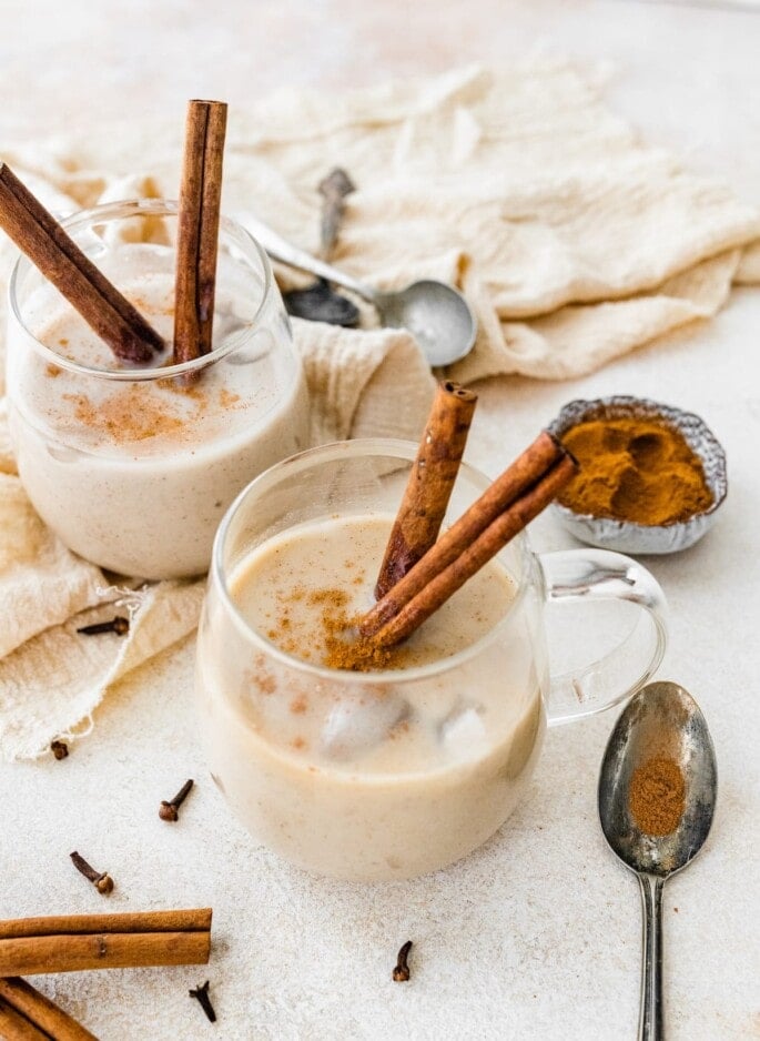 Two glasses of dairy free eggnog with cinnamon sticks.