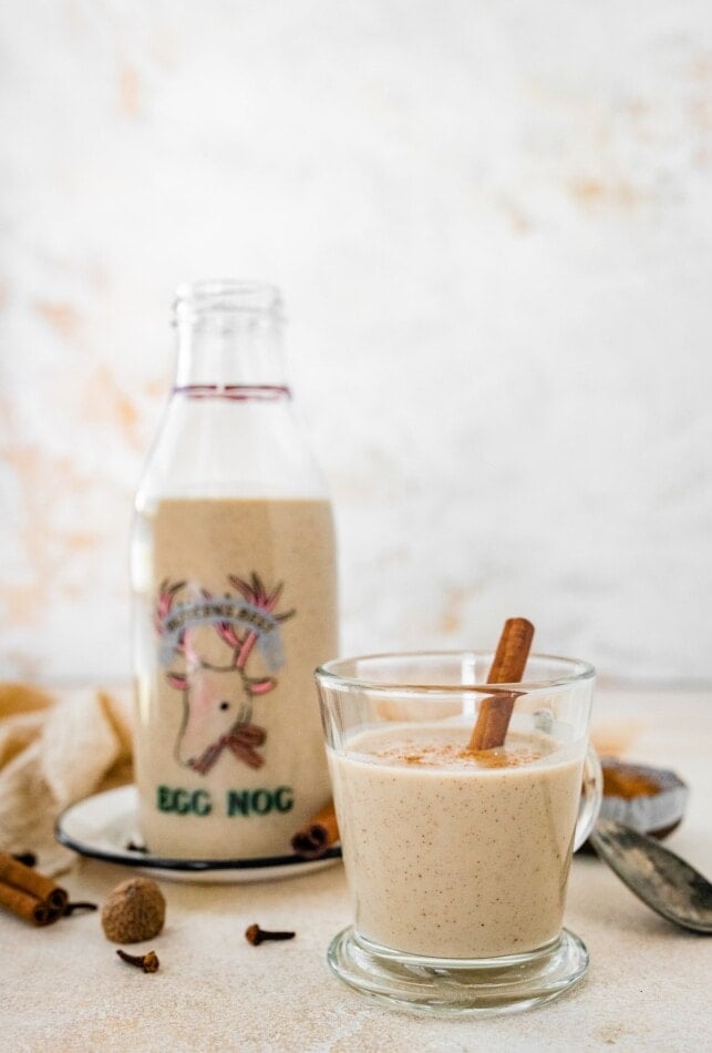 A glass of dairy free eggnog next to a jug.