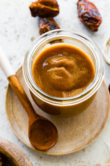 A glass jar of date caramel near a wooden spoon.