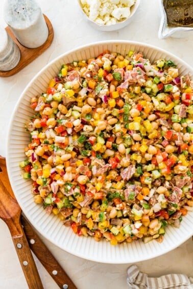 Colorful dense bean salad with beans, salami, feta, and veggies in a white serving bowl.