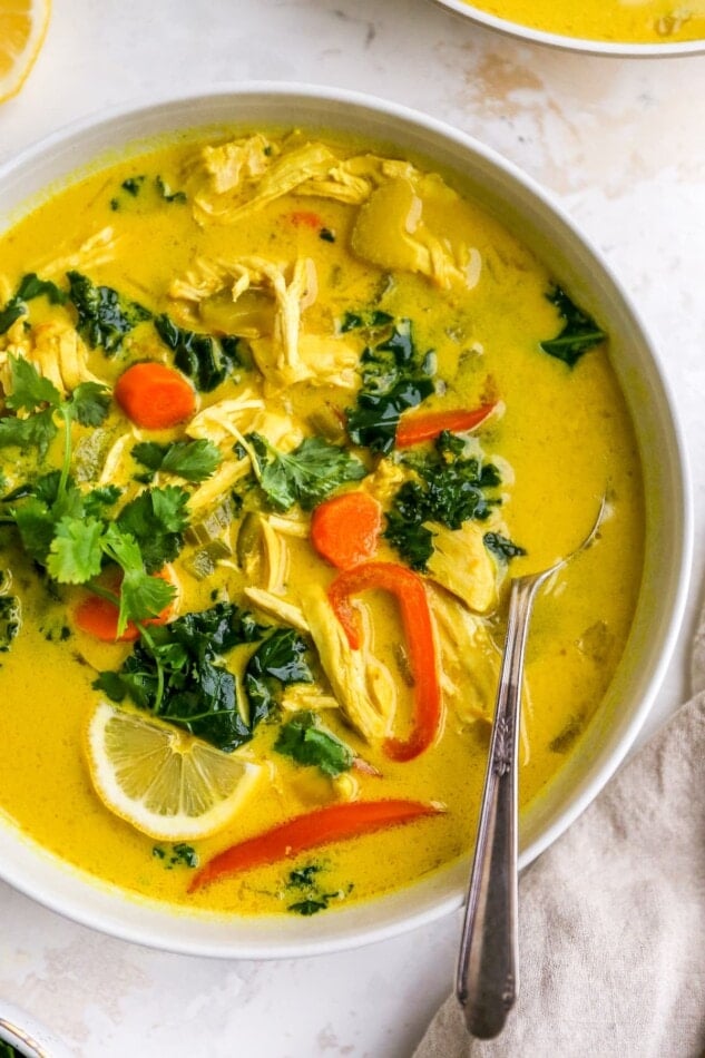 An overhead photo of a bowl of detox soup topped with fresh cilantro and lemon wedges. A spoon rests in the bowl.