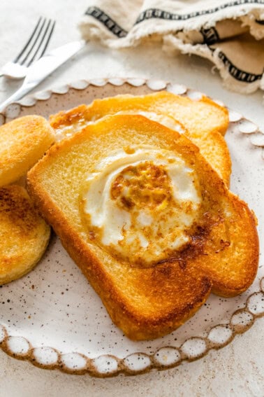 A slice of toast on a plate with the center cut out of it. A cooked egg is in the center of the slice of bread.