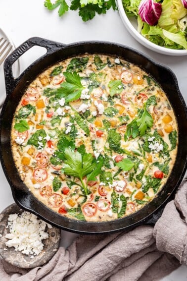 An egg white frittata in a cast iron skillet. The frittata is garnished with fresh herbs and feta cheese.
