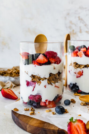 Two glass cups of fruit and yogurt parfaits. The cups are layered with fruit, yogurt, granola, then yogurt again and more fruit on top.