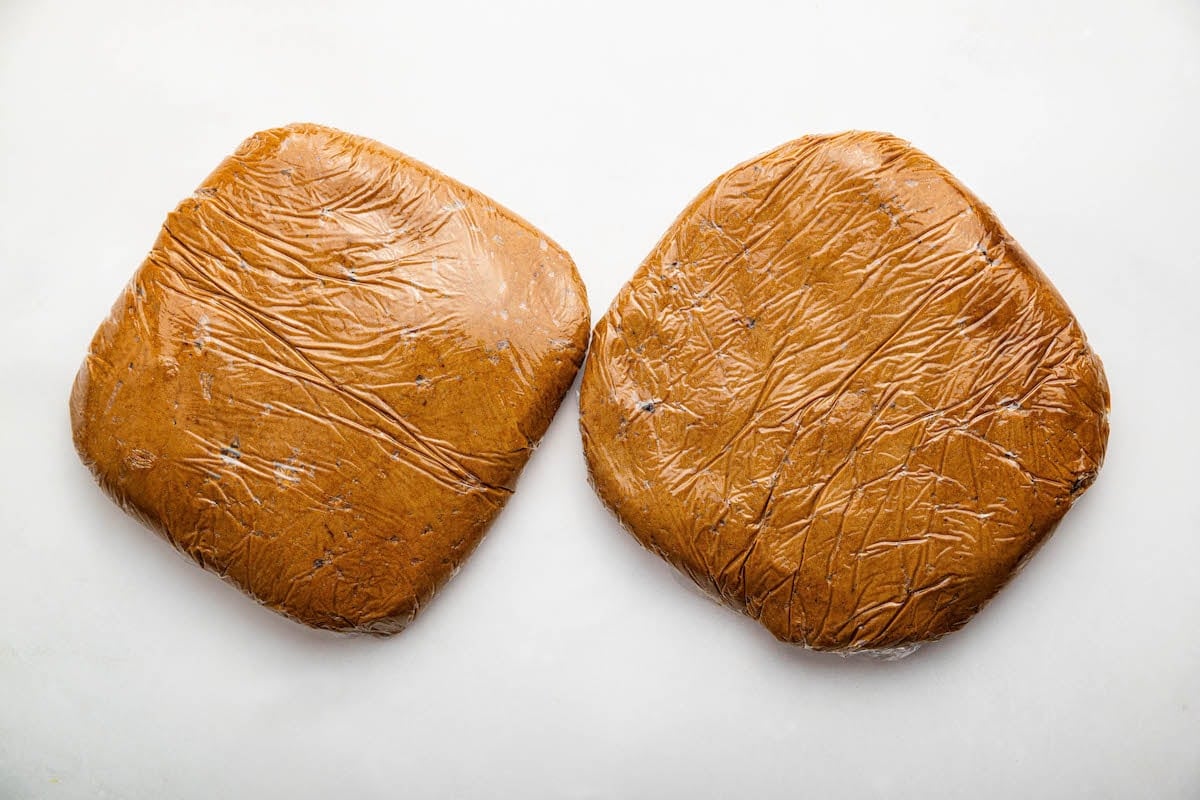 Two square blocks of gingerbread cookie dough in plastic wrap.