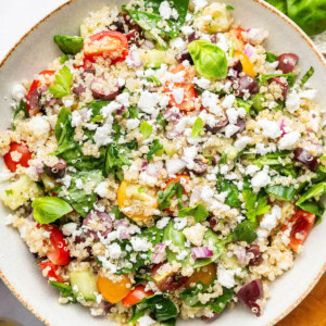 Greek quinoa salad in a tan serving bowl topped with crumbled feta cheese.