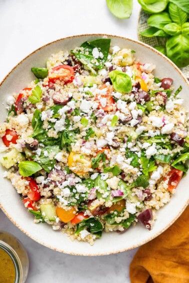 Greek quinoa salad in a tan serving bowl topped with crumbled feta cheese.