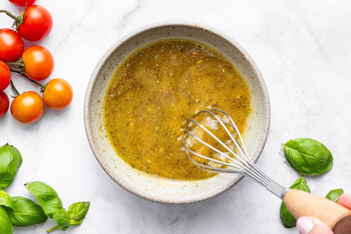 A woman's hand whisking together the Greek dressing in a small bowl.