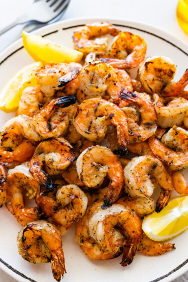 A large plate full of grilled shrimp with lemon wedges on the side.
