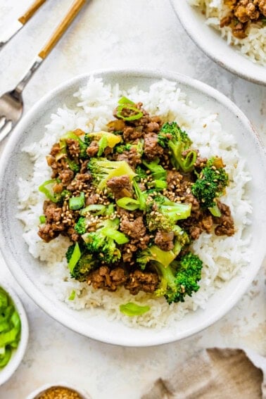 Ground beef and broccoli served on a bed of white rice, topped with sesame seeds and green onions.