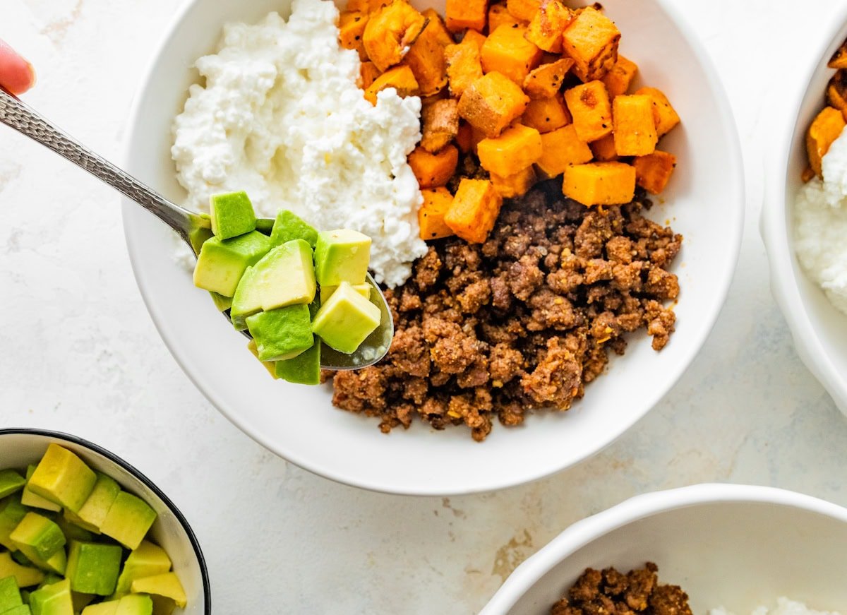 Ground beef, roasted sweet potatoes, cottage cheese and chopped avocado in a white bowl.