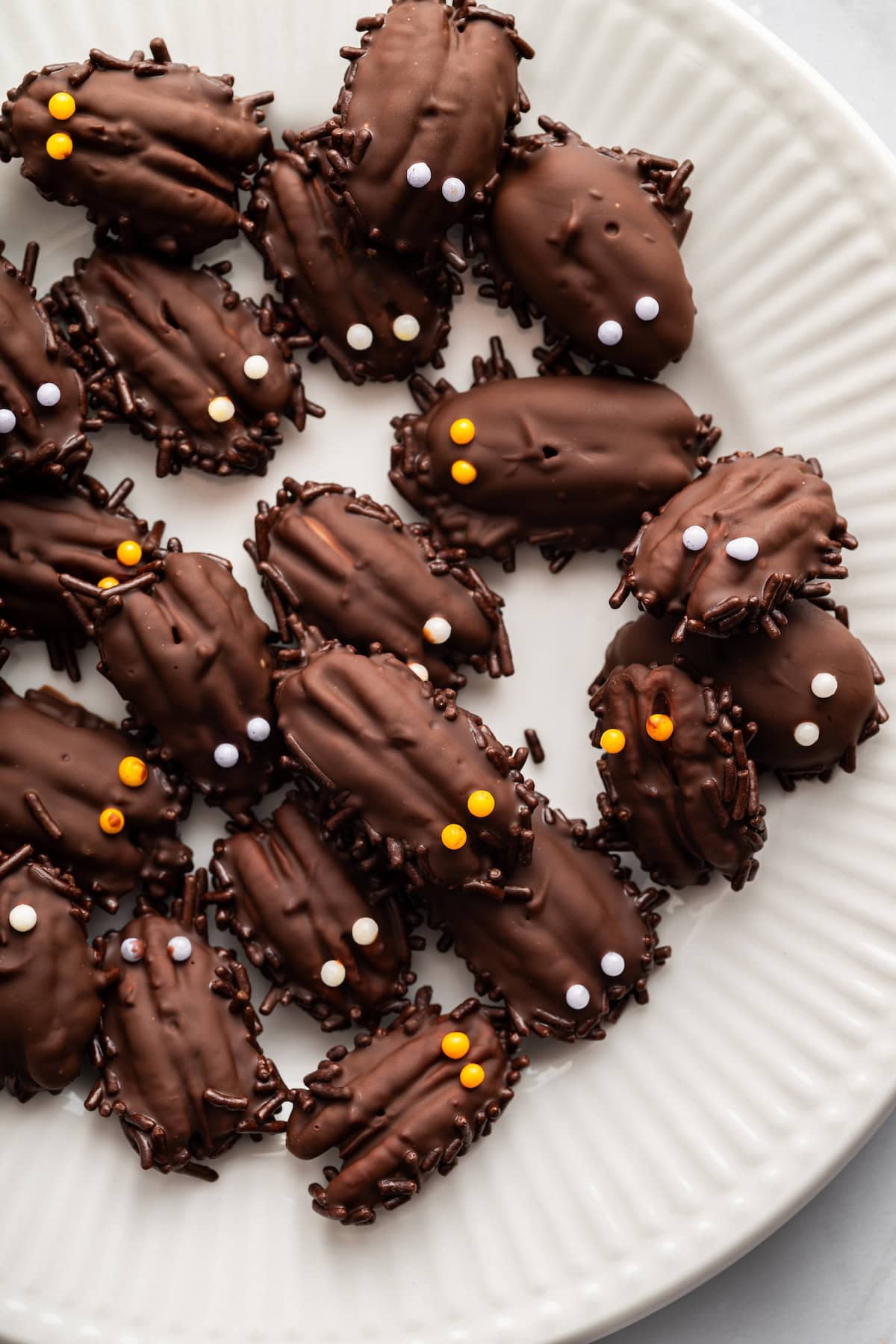 Chocolate-dipped pecans decorated with Halloween sprinkles arranged on a white plate.