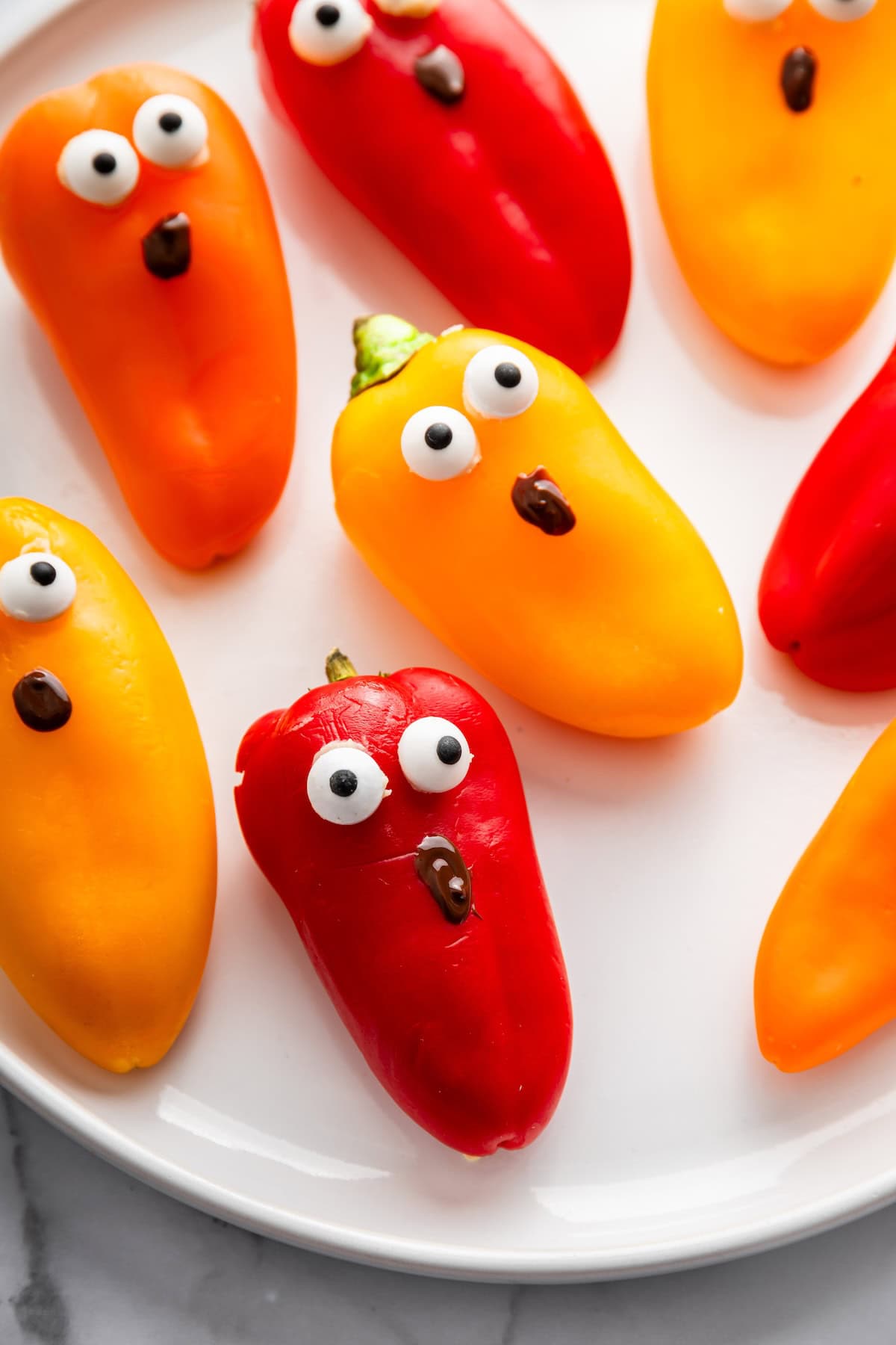 Mini bell peppers in orange, red, and yellow decorated with candy eyes to look like ghosts.