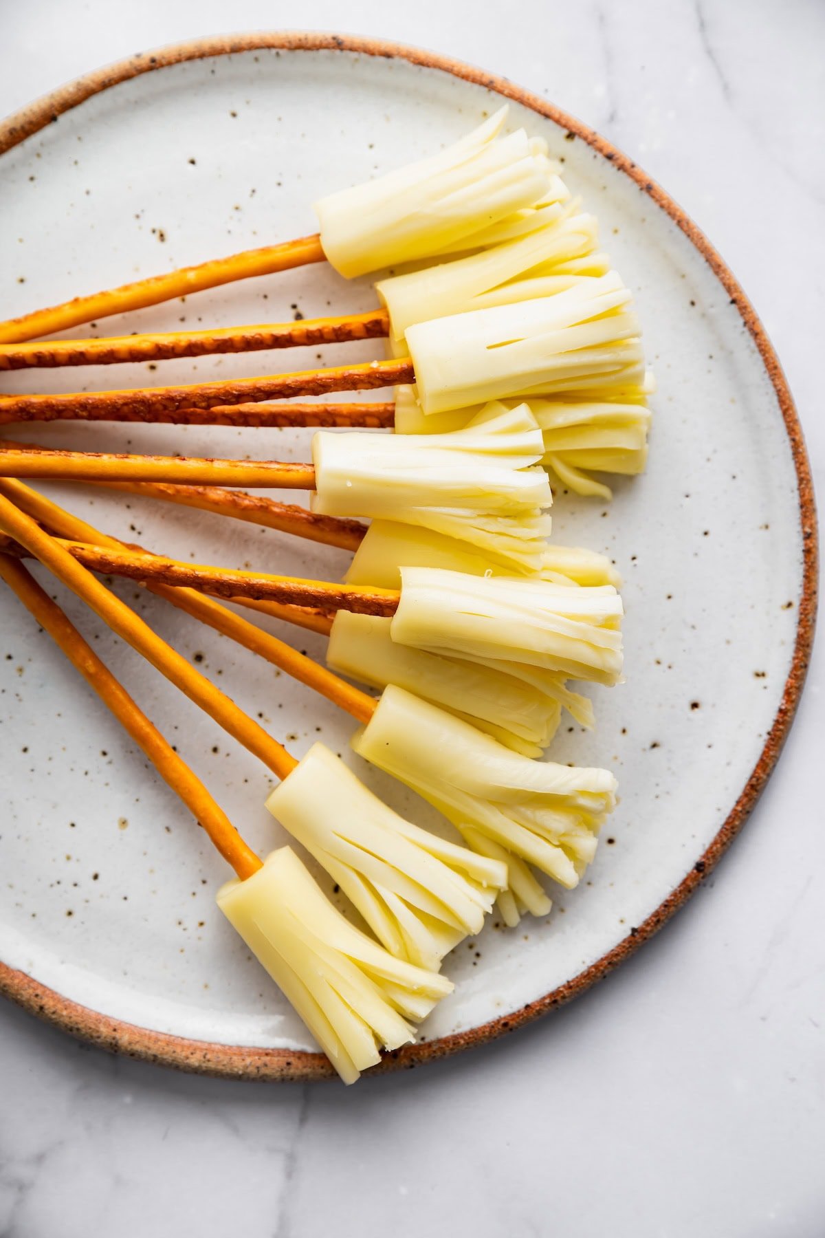 Mozzarella string cheese broomsticks with pretzel stick handles on a white plate.