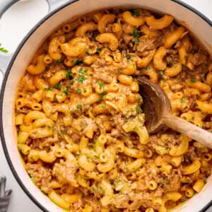 Healthy hamburger helper garnished with fresh herbs, in a large pot with a wooden serving spoon.