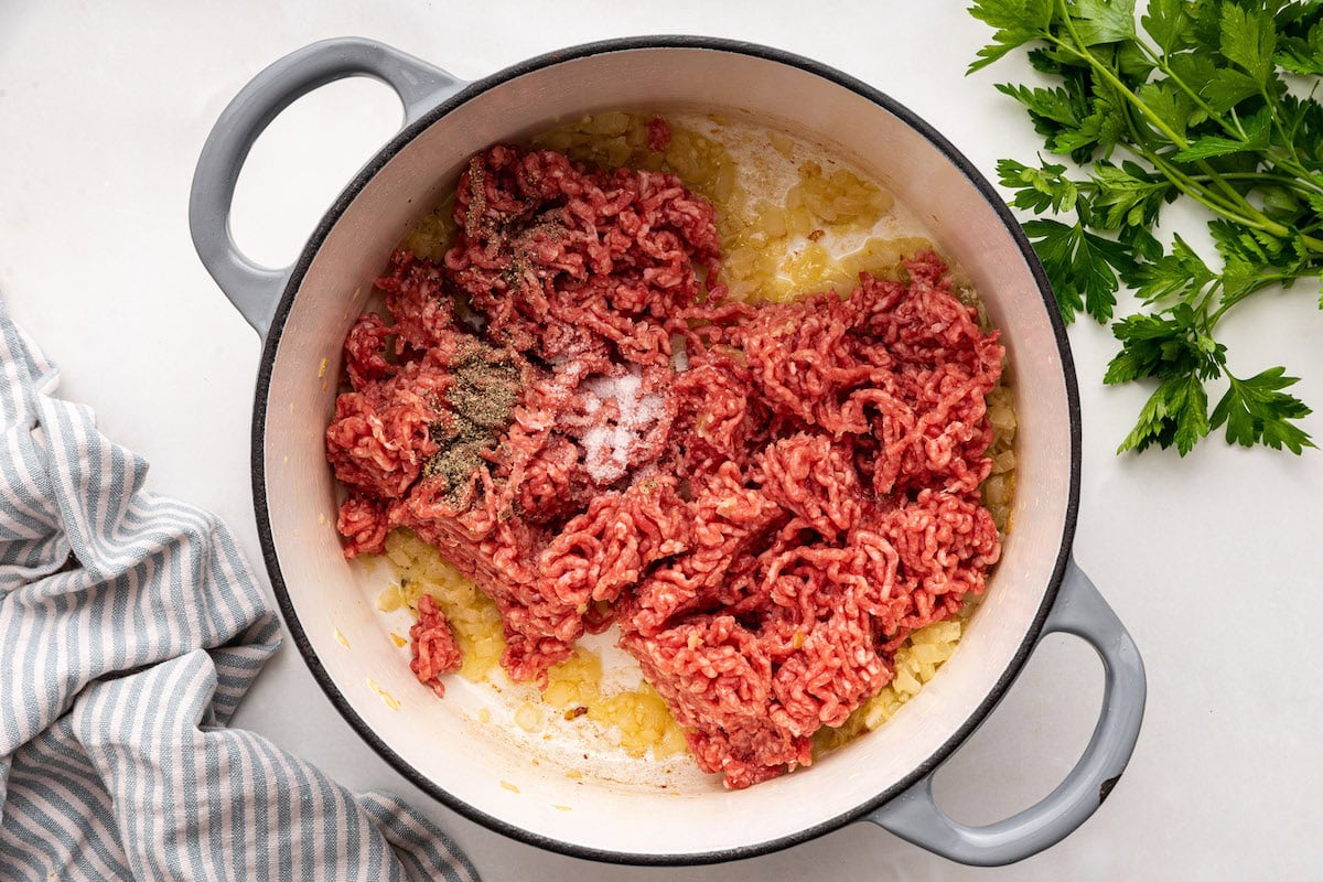 Ground beef and seasonings added to a large pot with sauteed onions and garlic.