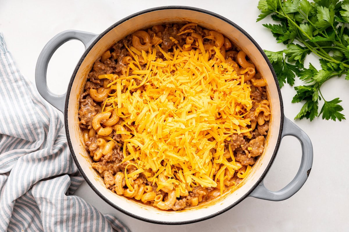 Shredded cheese added to the top of a healthy hamburger helper in a large pot.