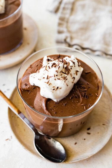 A hard boiled egg chocolate pudding in a glass container, topped with whipped cream and chocolate shavings.