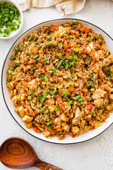 Bowl of homemade chicken fried rice topped with chopped green onions and served on a white table.
